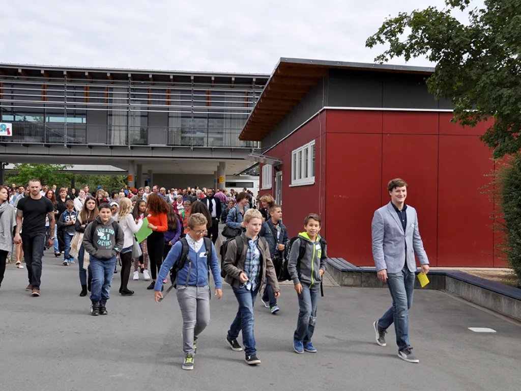Kinder werden über den Schulhof zur Sporthalle begleitet.